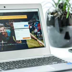 Close-up of a laptop displaying Twitter login page, accompanied by a smartphone and a potted plant in a bright workspace.